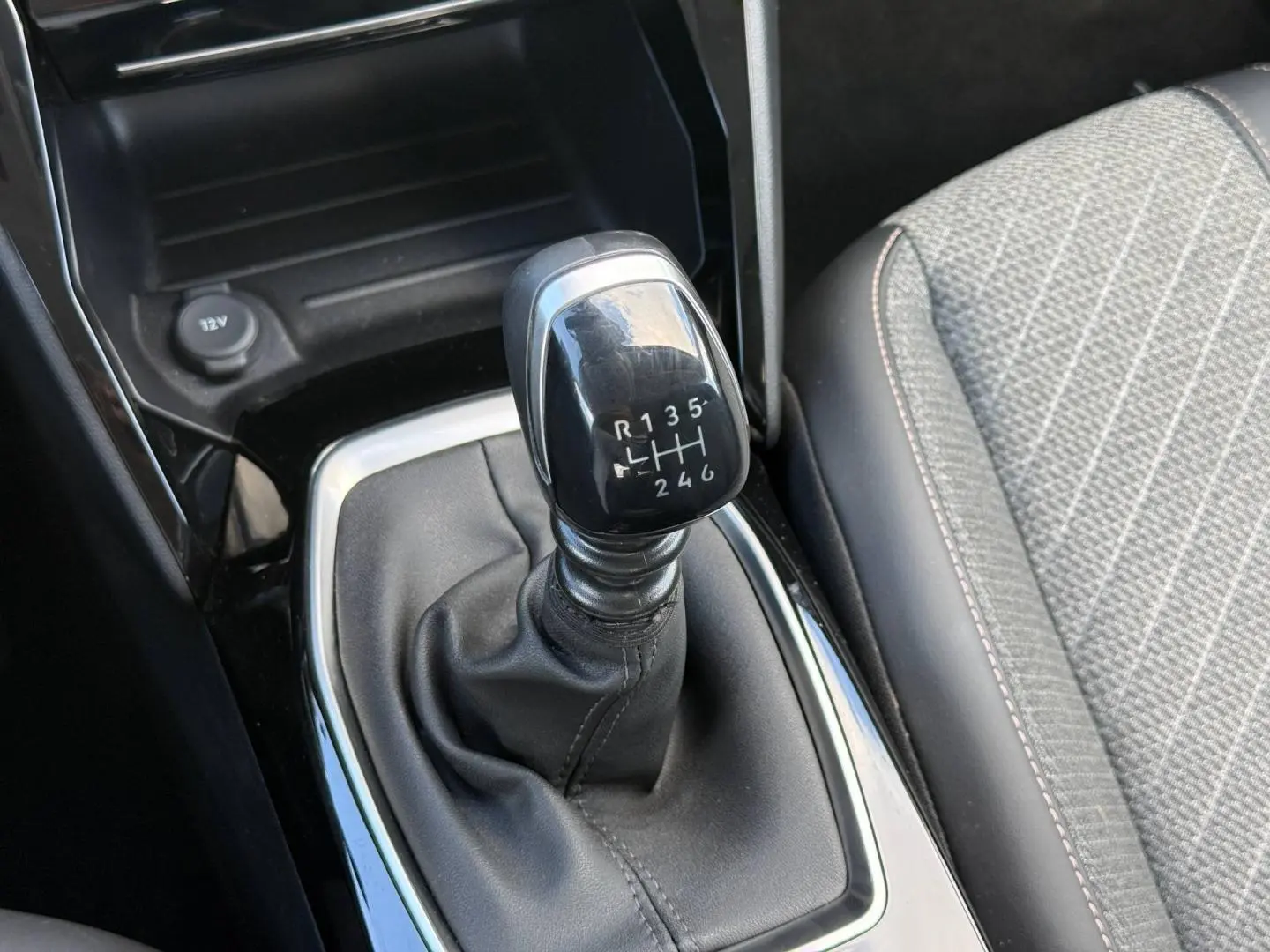 Le levier de vitesse manuel noir de la Peugeot 208 1.2 100ch Allure avec sellerie tissu gris et surpiqûres contrastées.