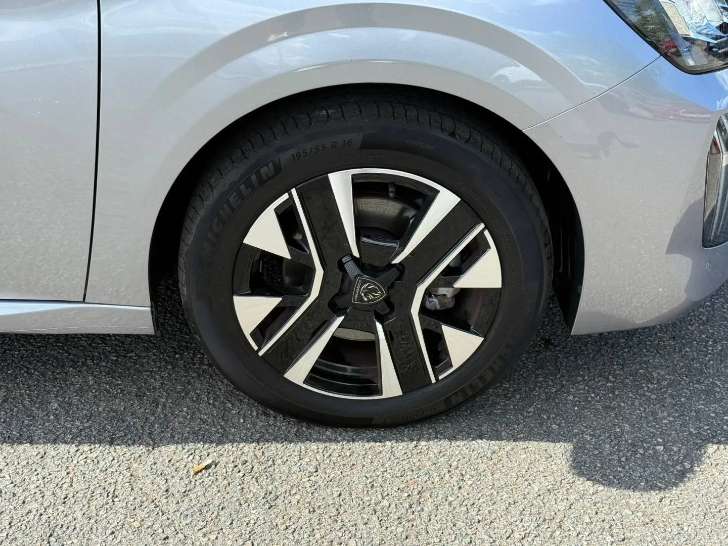 Gros plan sur la roue avant droite d’une Peugeot 208 gris Artense avec jante alu au design moderne.