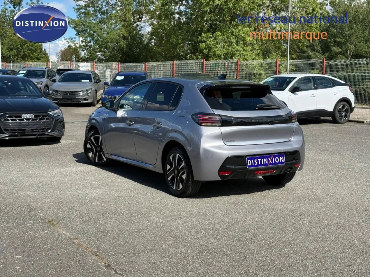 Vue 3/4 arrière droite d'une Peugeot 208 gris Artense avec jantes alliage, sur un parking extérieur ensoleillé.