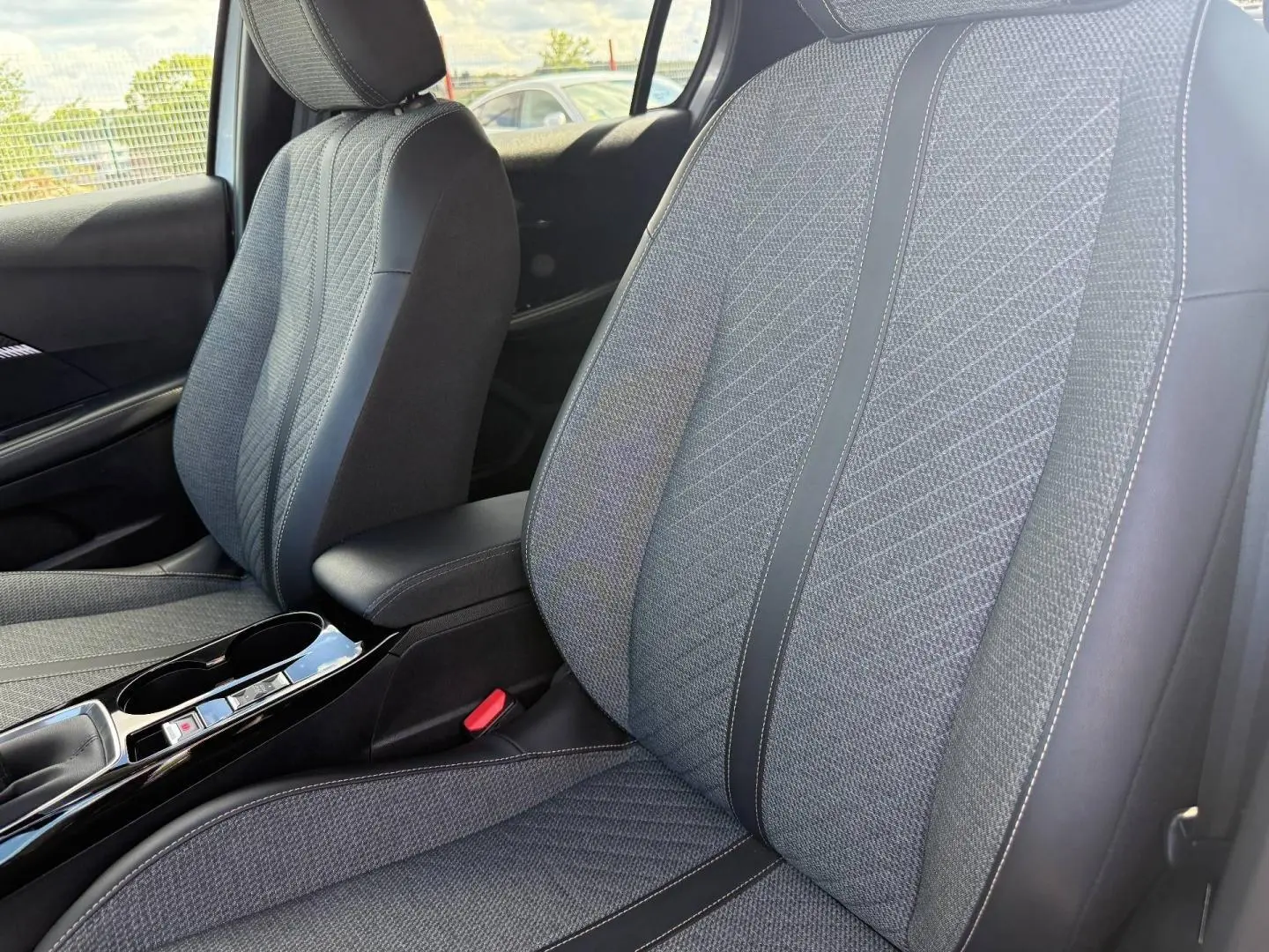 Vue rapprochée des sièges avant gris tissu et cuir avec accoudoir central et console brillante d'une Peugeot 208 2025.