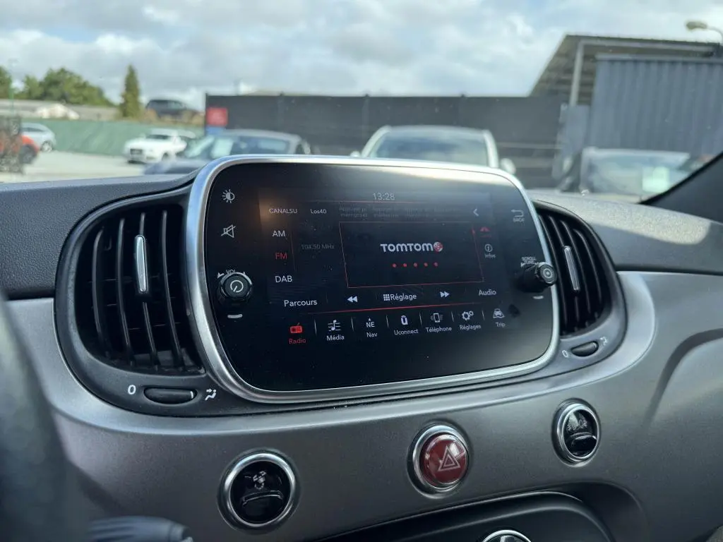 Écran tactile central 7'' avec interface TomTom sur tableau de bord gris satiné d'une Abarth 500 blanche, vue intérieure frontale.