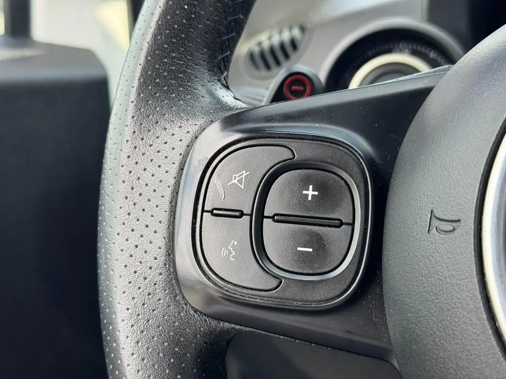 Gros plan sur les commandes de volume et de sourdine du volant cuir perforé de l'Abarth 500 blanc 2021.