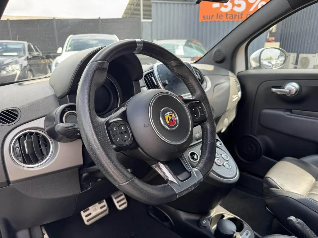 Intérieur de l'Abarth 500 blanc, vue côté conducteur sur le volant cuir avec logo Abarth et tableau de bord gris satiné.