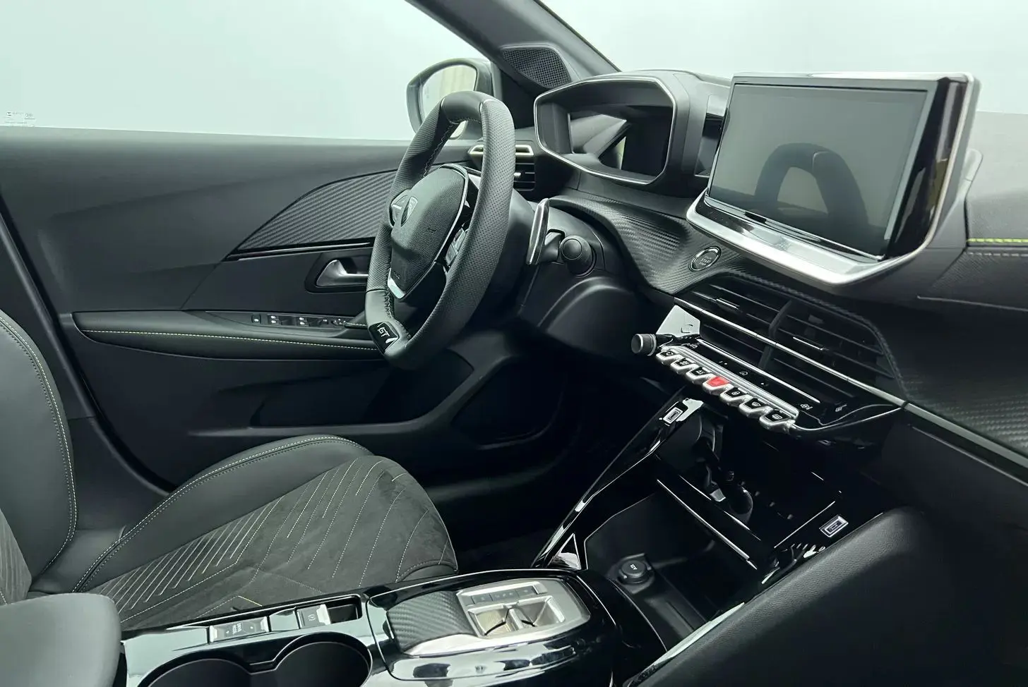 Vue intérieure côté conducteur de la Peugeot 208 1.2 Hybrid 136 GT 2025, avec tableau de bord noir et écran tactile central.