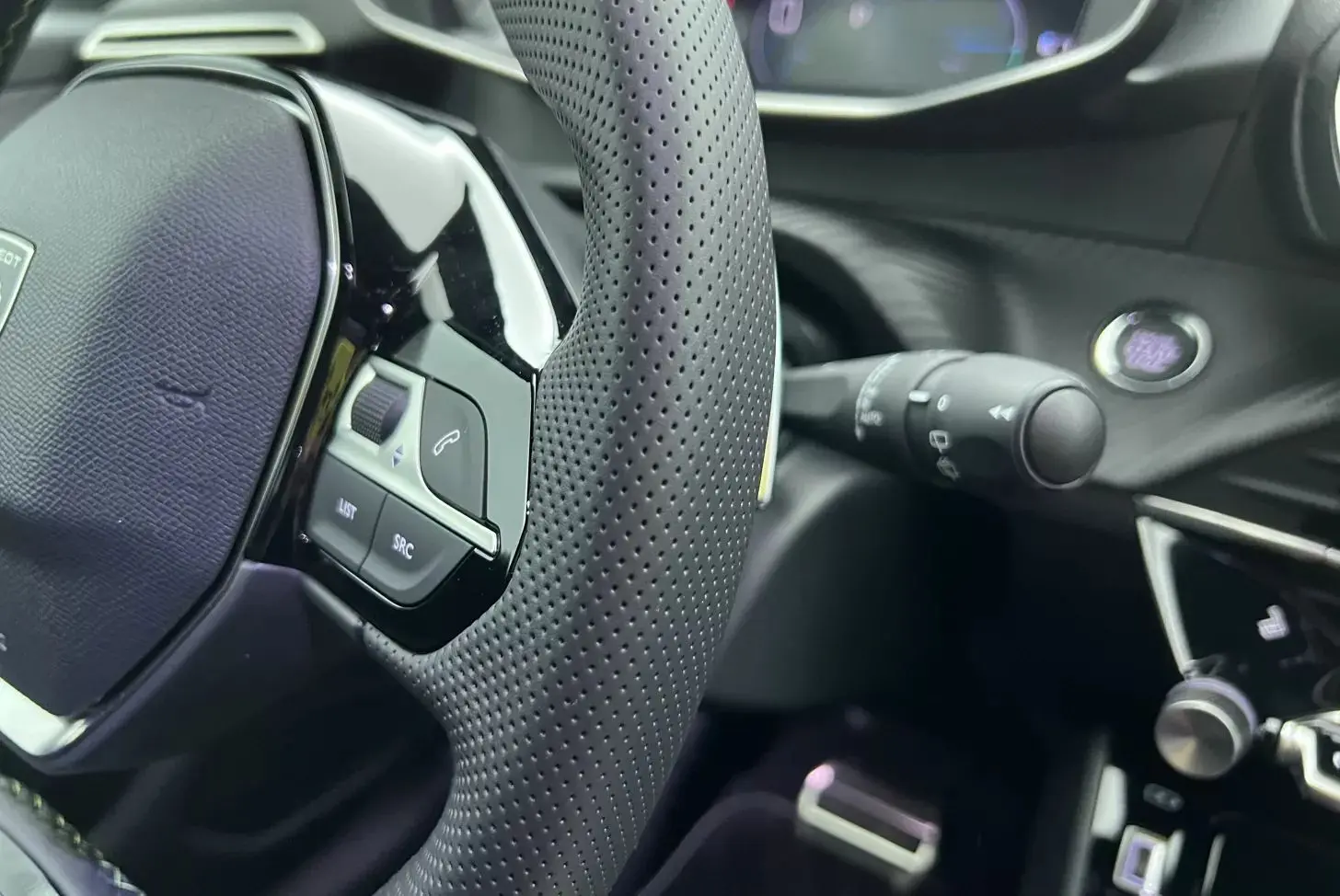 Gros plan sur le volant perforé et les commandes intégrées du tableau de bord noir de la Peugeot 208 1.2 Hybrid 136 GT.