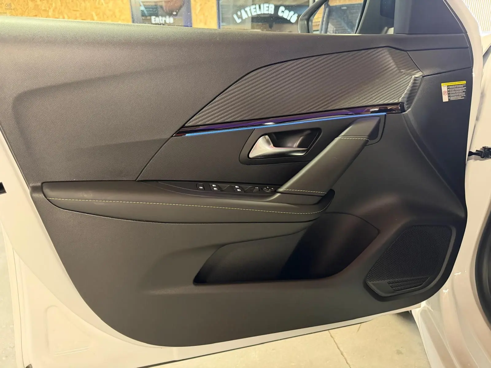 Vue intérieure du panneau de porte avant gauche noir avec surpiqûres et insert effet carbone sur Peugeot 208 blanc 2025.