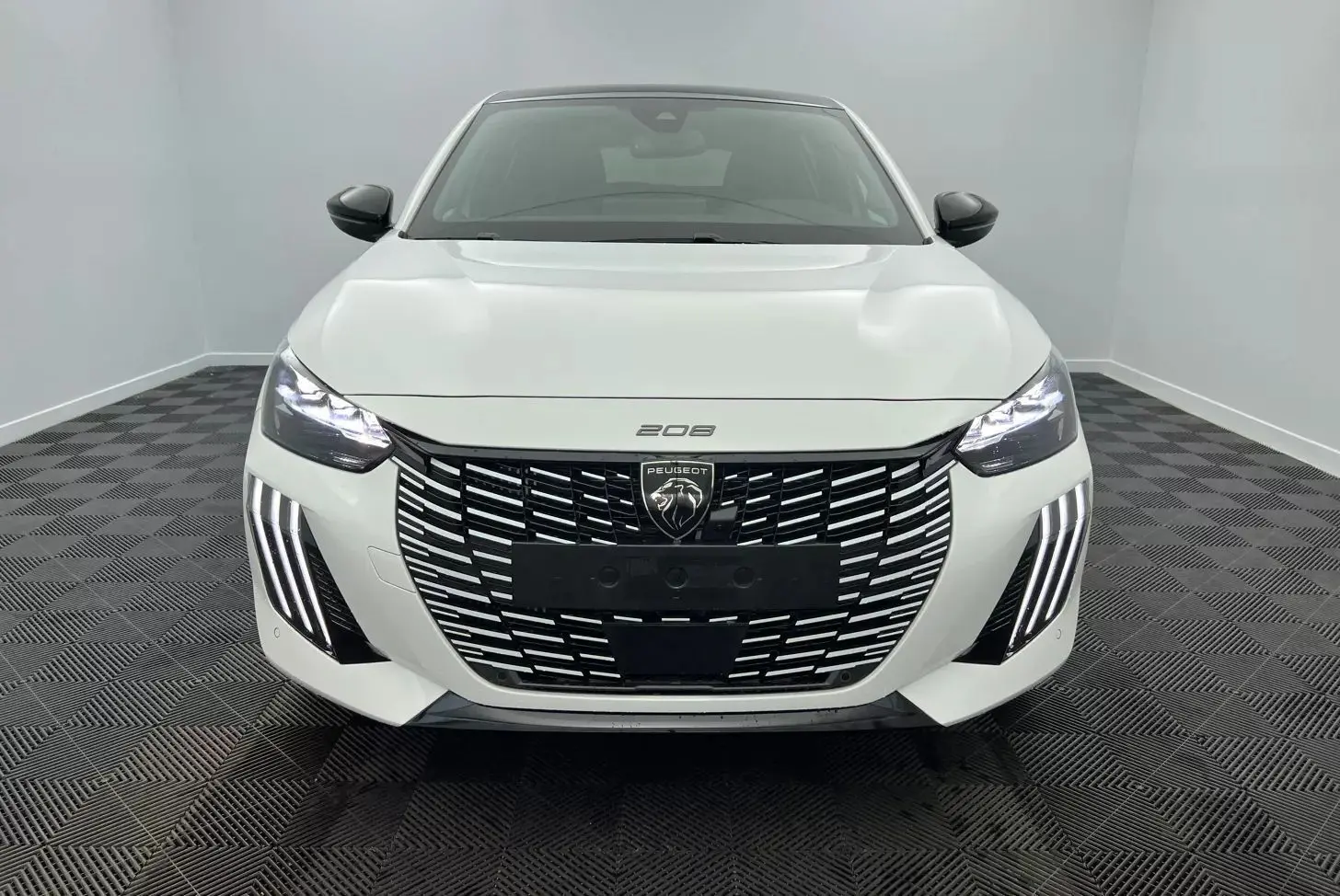 Peugeot 208 1.2 Hybrid 136 GT blanc vue de face, avec calandre large et feux LED distinctifs allumés.
