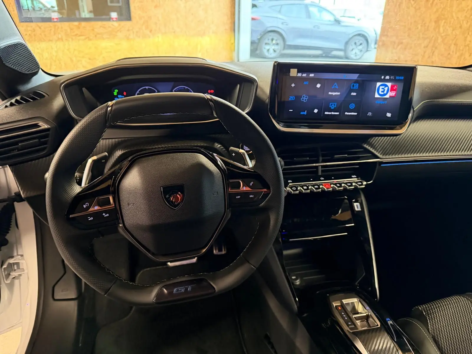 Vue intérieure du poste de conduite de la Peugeot 208 1.2 HYBRID 136 GT blanche, avec volant compact et écran tactile central.