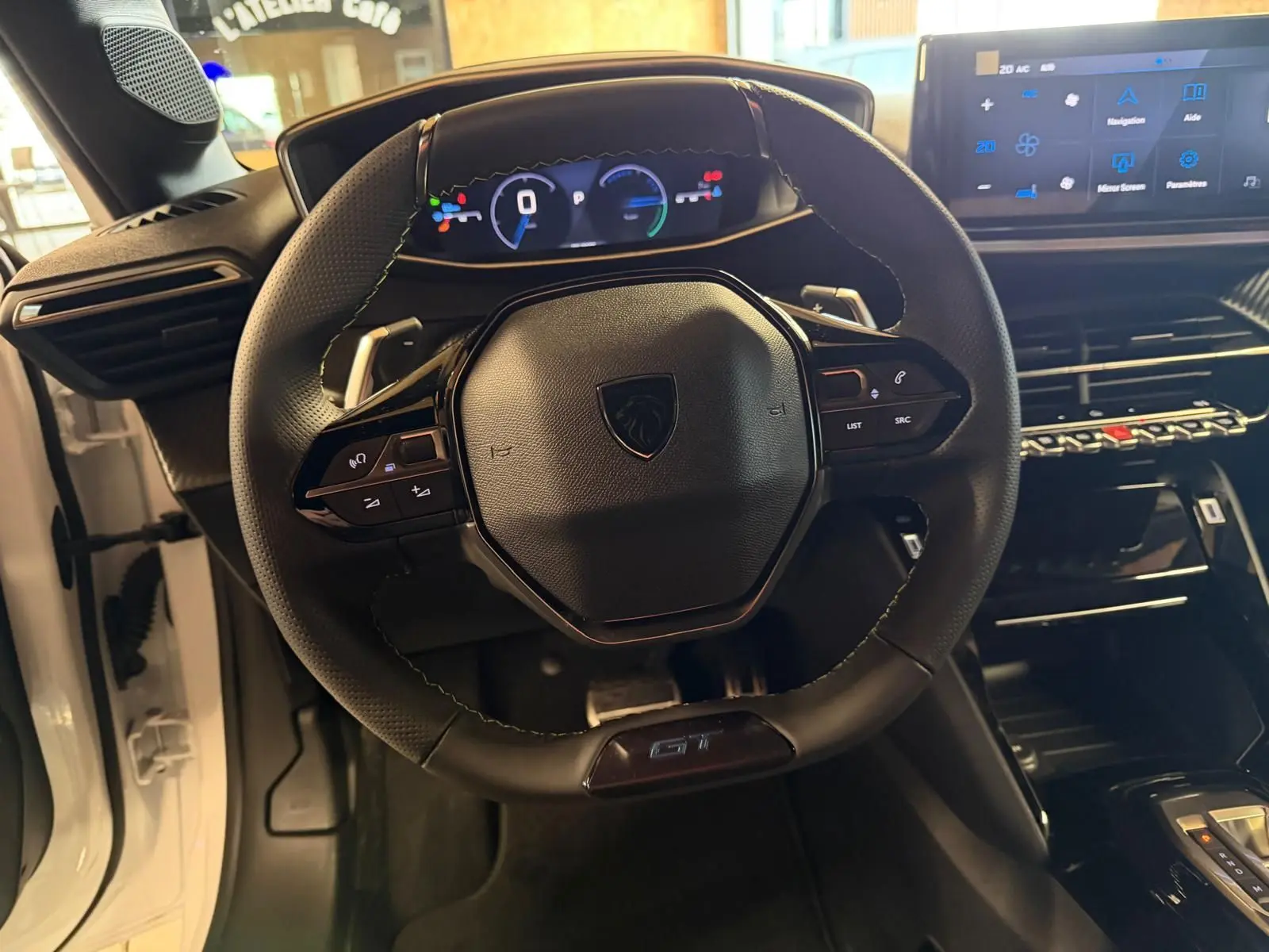 Vue intérieure centrée sur le volant noir GT et le tableau de bord numérique de la Peugeot 208 blanche 1.2 Hybrid 136.