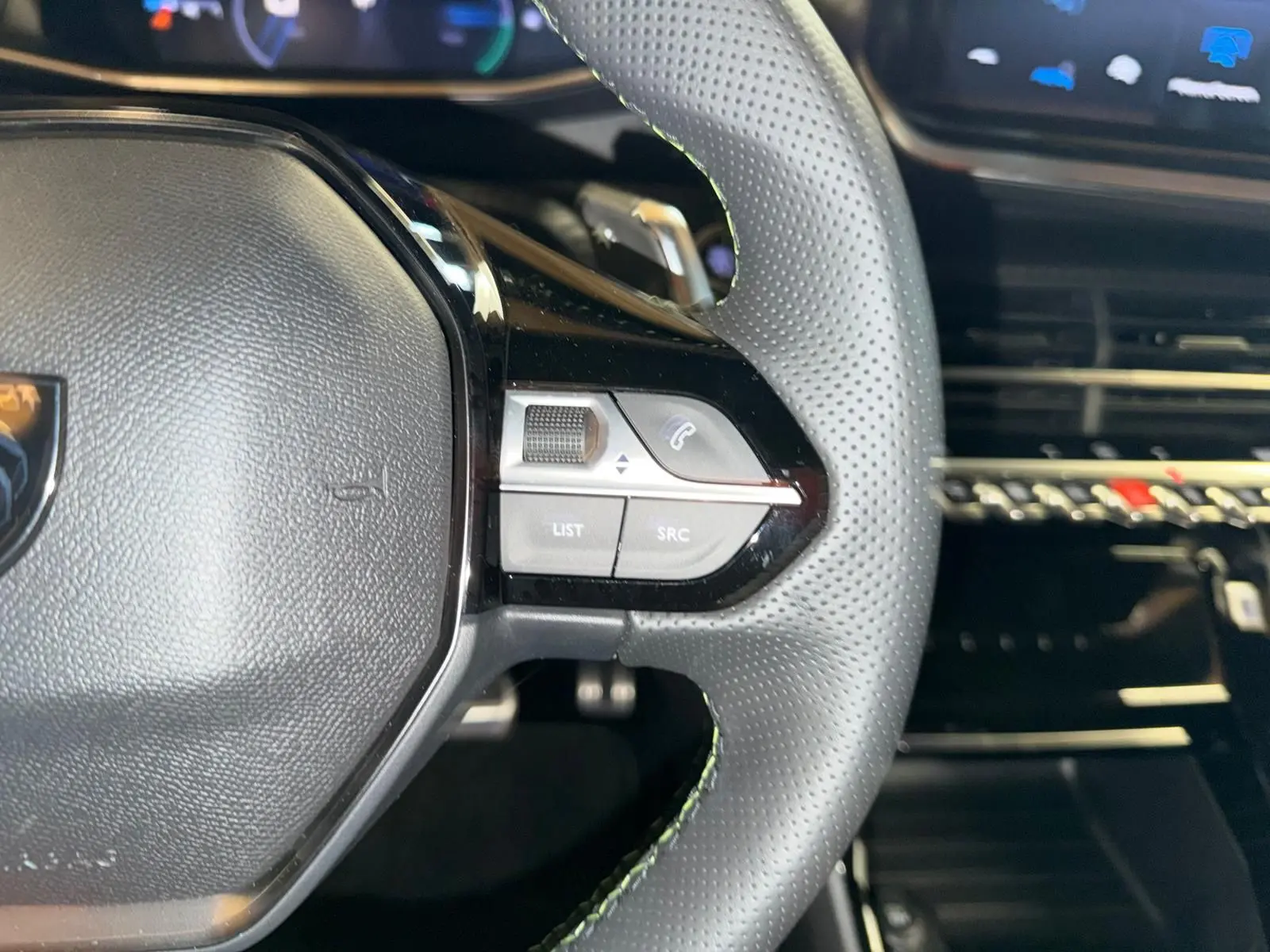 Gros plan sur le volant perforé de la Peugeot 208 1.2 HYBRID 136 GT avec commandes intégrées côté droit, intérieur noir.