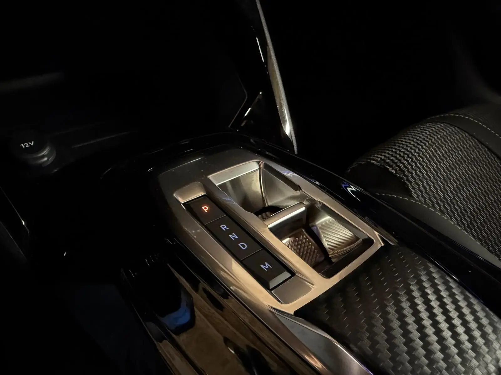 Gros plan sur la console centrale avec la boîte automatique de la Peugeot 208 1.2 Hybrid 136 GT, intérieur noir et détails carbone.