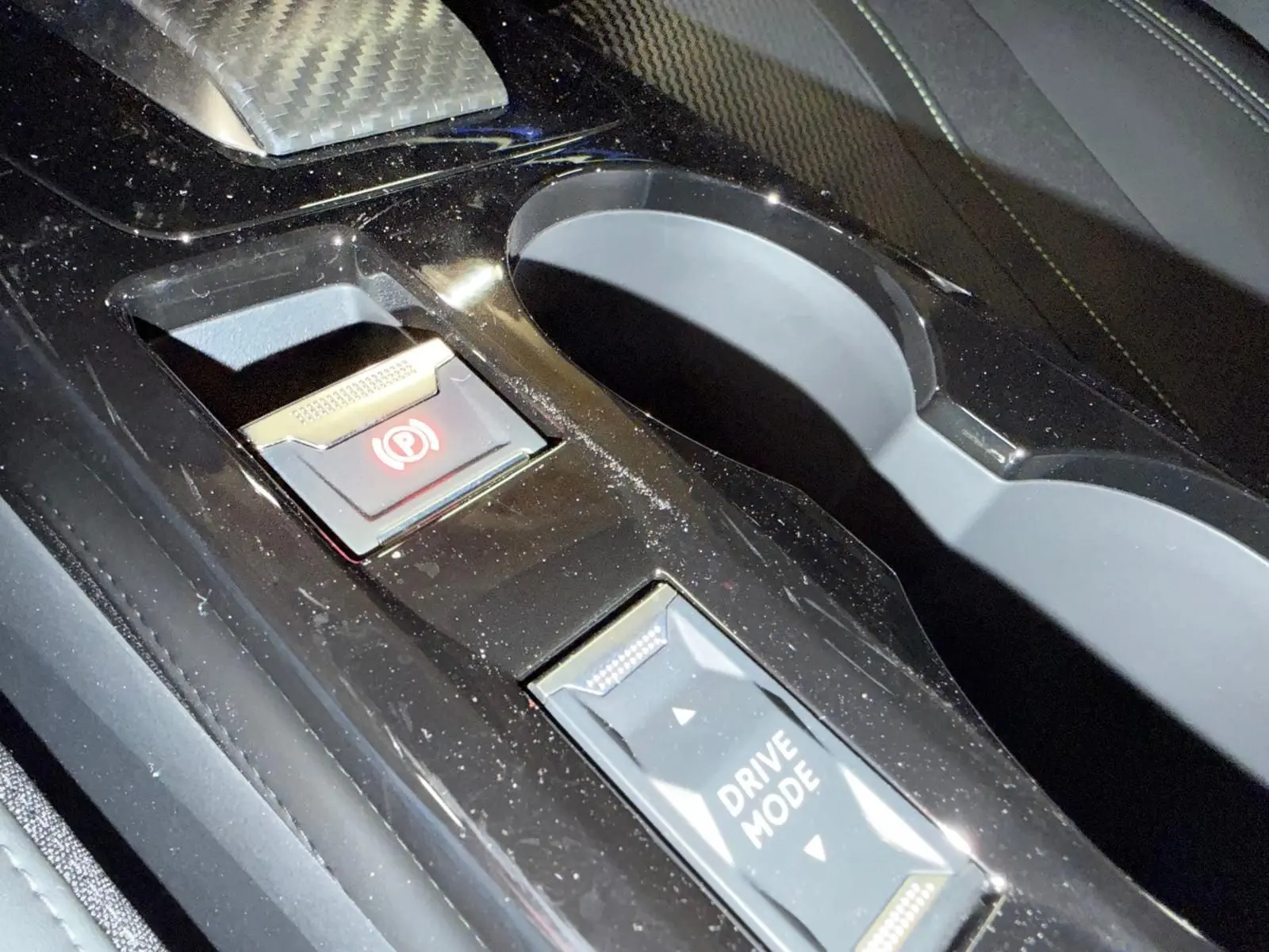 Gros plan sur la console centrale noire de la Peugeot 208 1.2 Hybrid 136 GT avec bouton frein à main électronique et sélection drive mode.