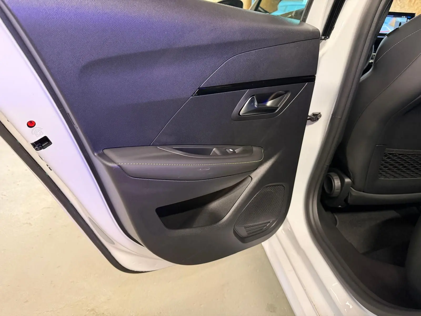 Vue intérieure de la porte arrière gauche noire avec surpiqûres vertes sur une Peugeot 208 blanche 1.2 Hybrid 136 GT 2025.