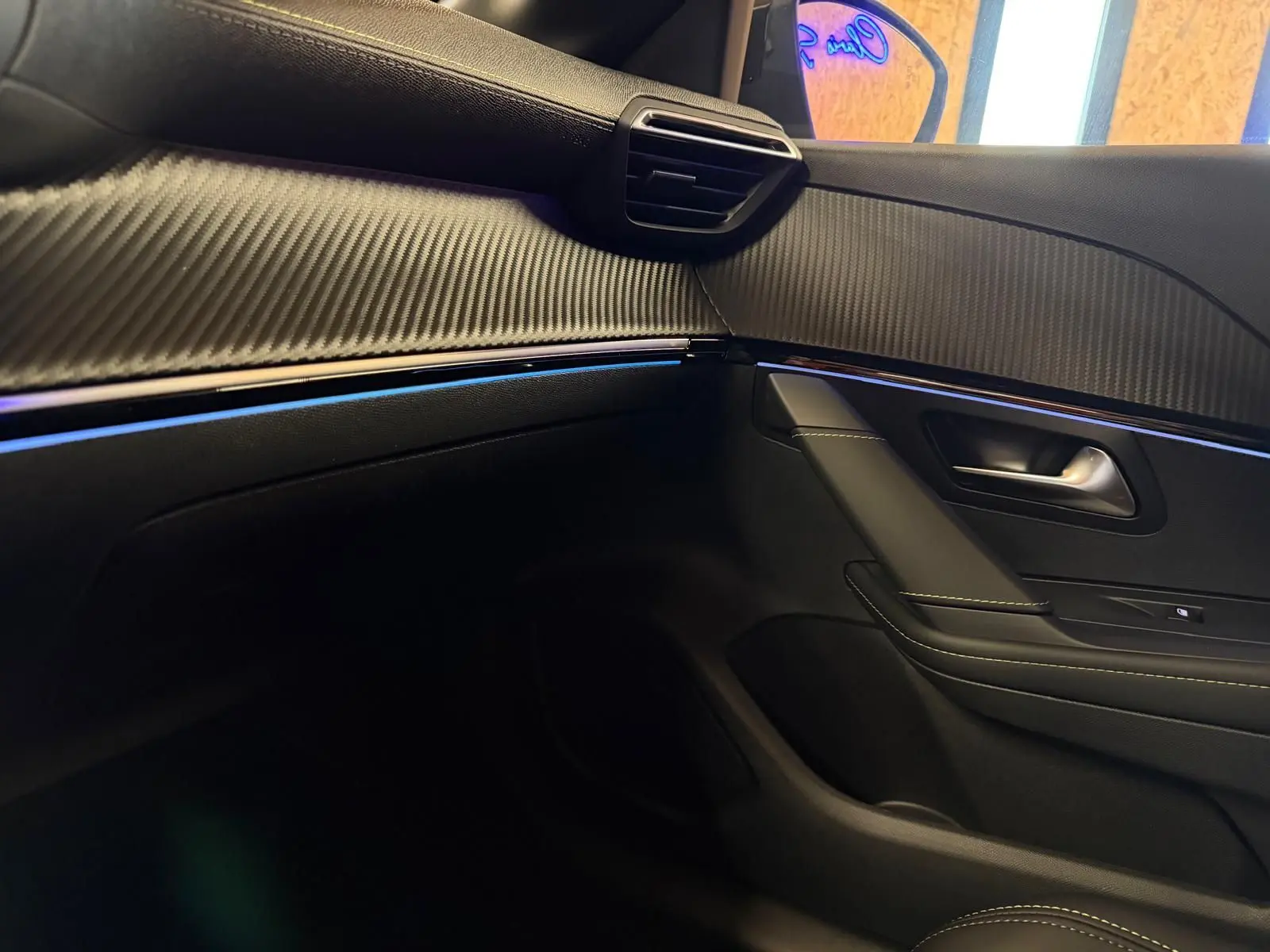 Détail de la porte côté passager de la Peugeot 208 1.2 Hybrid 136 GT 2025 en intérieur noir avec surpiqûres et insert effet carbone.