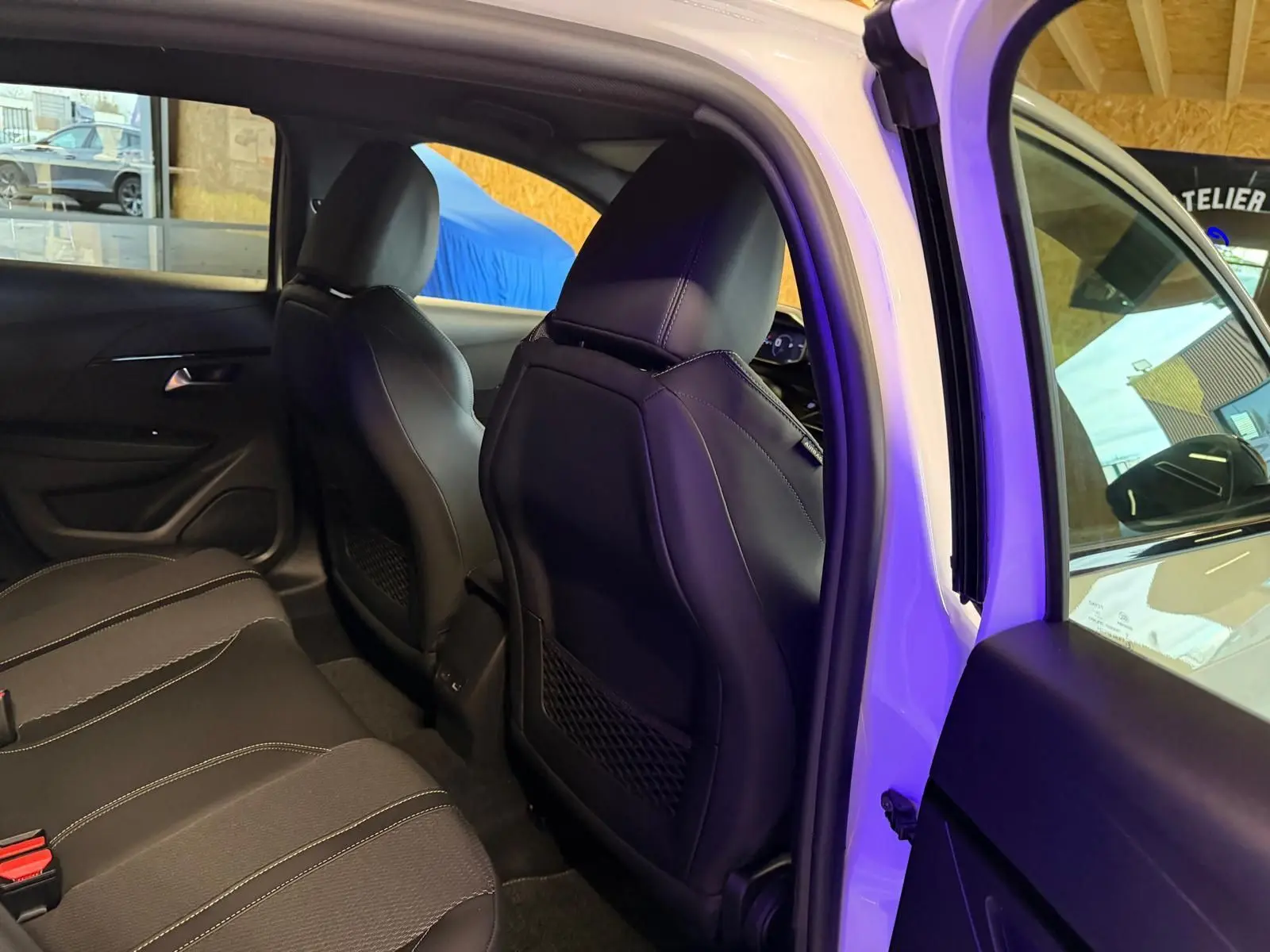 Vue intérieure arrière côté droit de la Peugeot 208 1.2 HYBRID 136 GT blanche, sièges noirs en tissu et cuir.