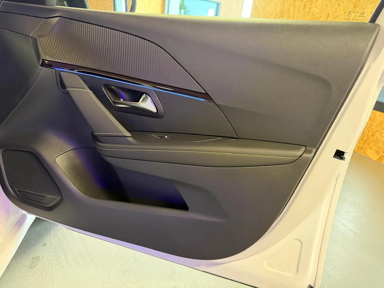 Vue intérieure côté gauche de la porte avant d’une Peugeot 208 1.2 Hybrid 136 GT blanche, avec garniture noire et surpiqûres contrastées.