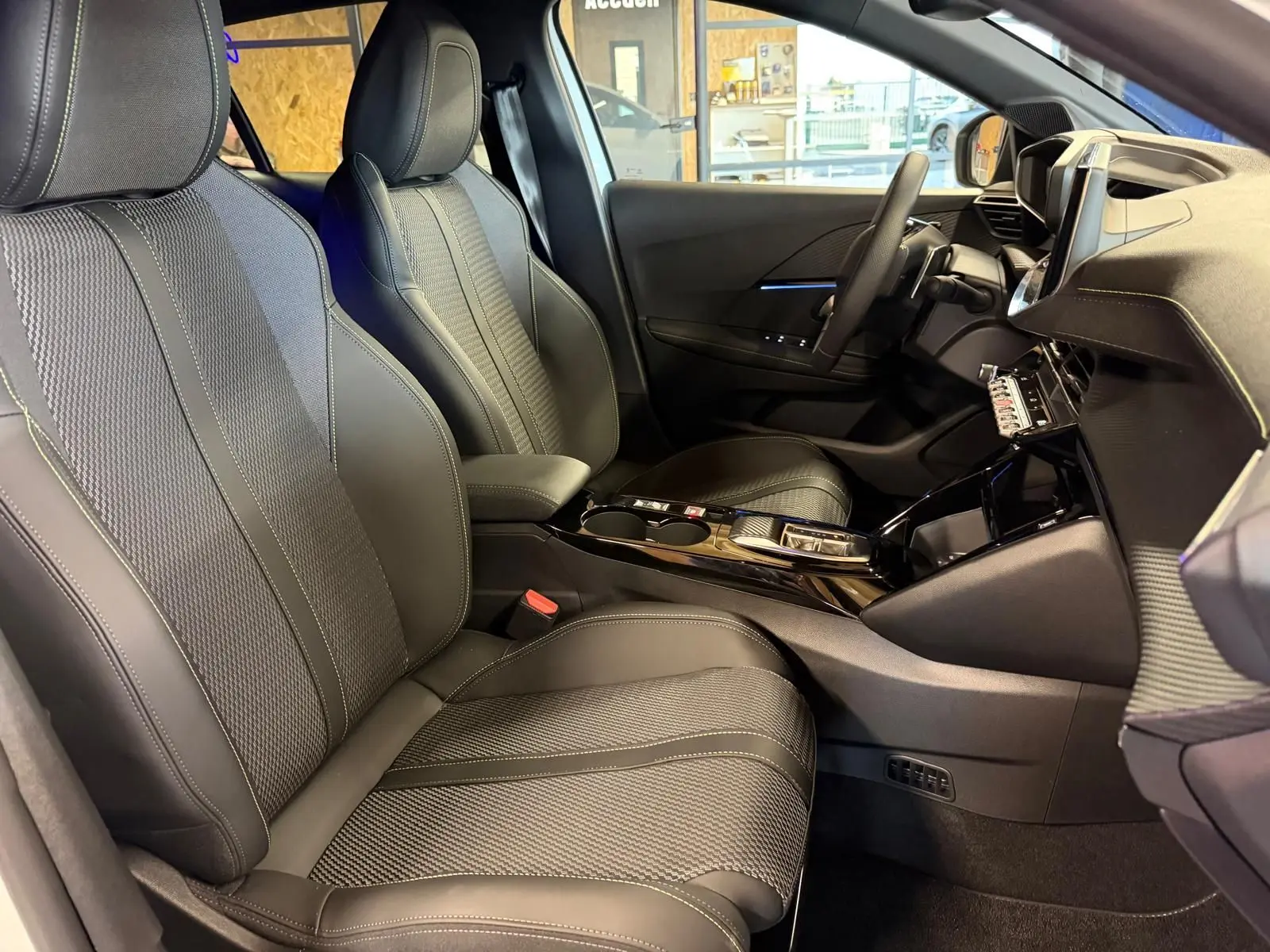Vue intérieure côté conducteur de la Peugeot 208 1.2 Hybrid 136 GT avec sièges tissu noir et console centrale brillante.