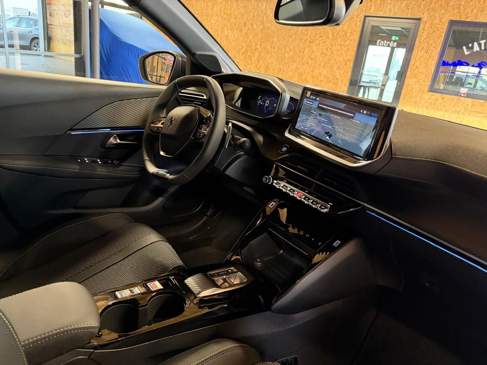 Vue intérieure côté conducteur du Peugeot 208 blanc 1.2 Hybrid 136 GT, mettant en valeur le tableau de bord numérique et l'écran tactile central.