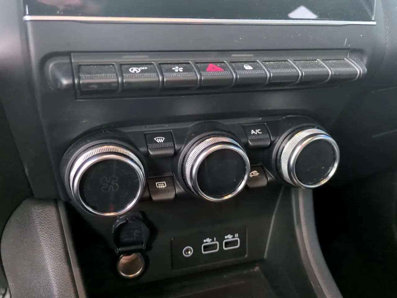 Gros plan sur la console centrale noire du Renault Captur 2024, avec commandes de climatisation et prises USB visibles.