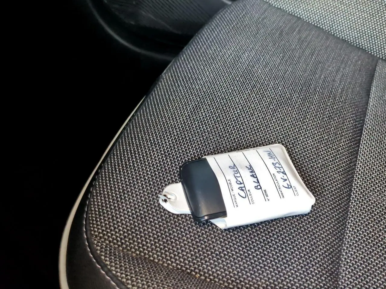 Gros plan sur la clé avec étiquette blanche posée sur le siège tissu gris foncé côté conducteur du Renault Captur blanc.
