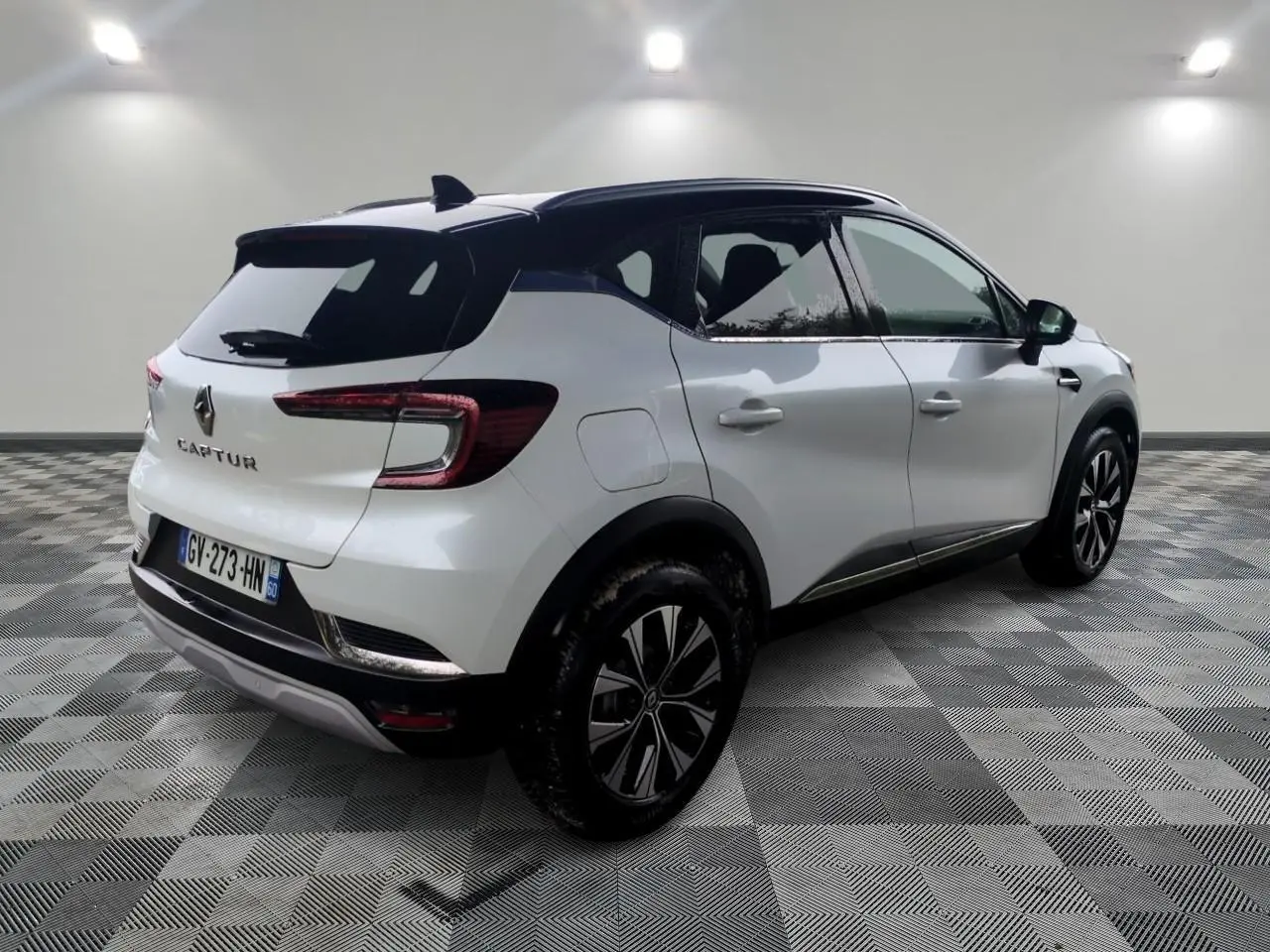 Vue 3/4 arrière droite d'un Renault Captur blanc 2024 avec toit noir et jantes alliage bicolores.