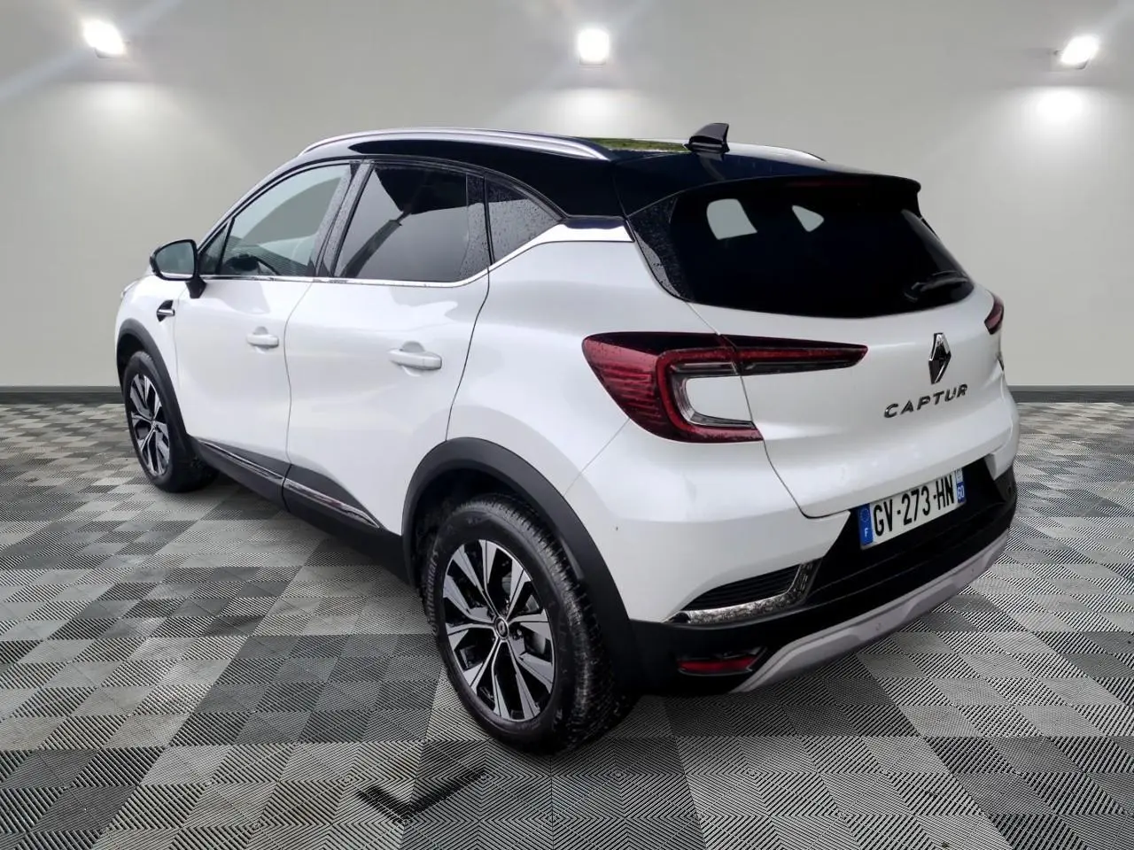Vue 3/4 arrière droite du Renault Captur blanc avec toit noir et jantes alliage bicolores sur fond neutre.