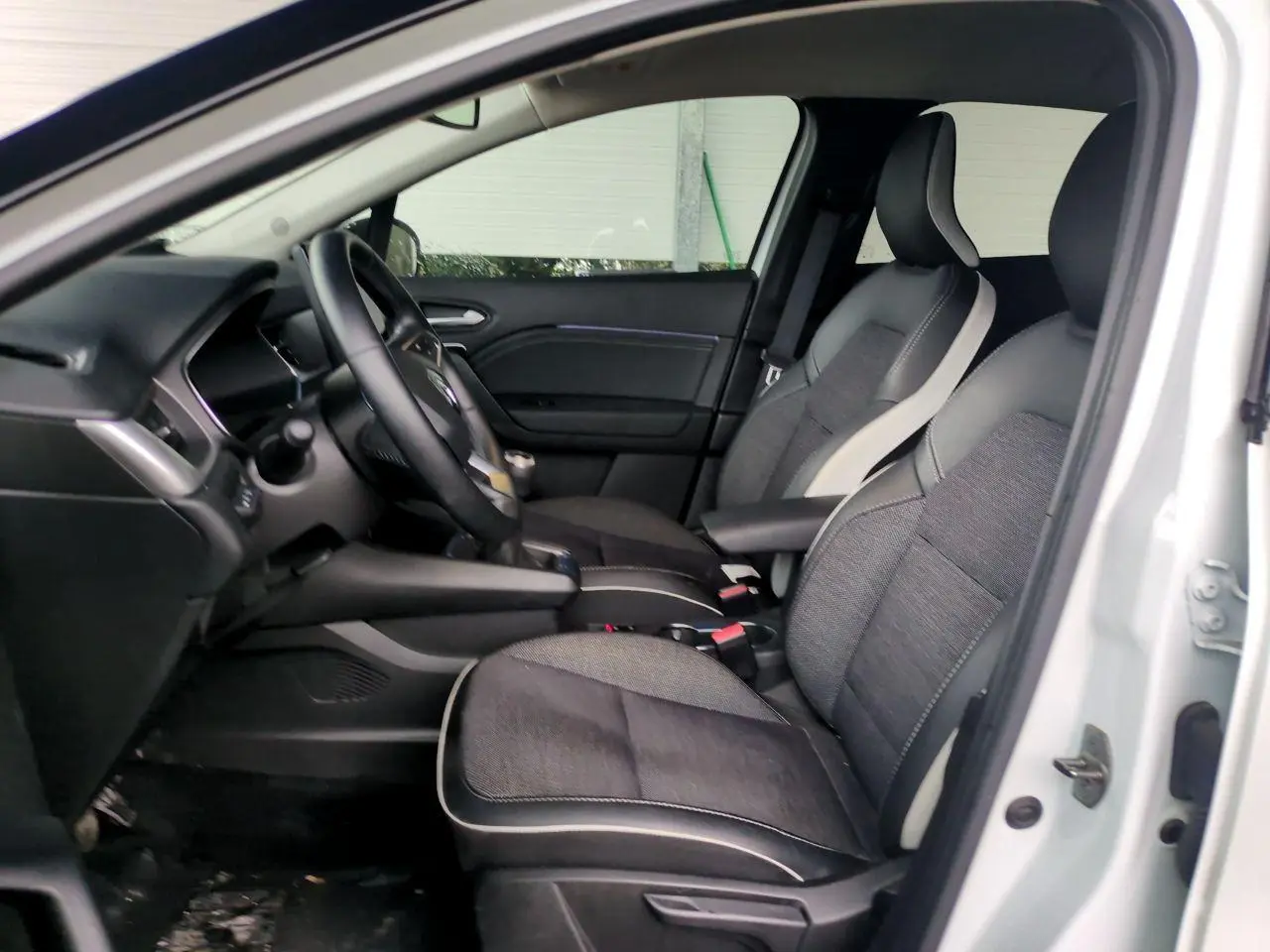 Vue intérieure côté conducteur du Renault Captur blanc 2024, sièges bi-matière gris et noir avec accoudoir central.