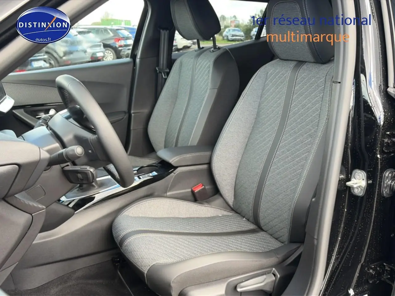 Vue intérieure côté conducteur du Peugeot 2008 noir 2025, mettant en valeur les sièges tissu gris et la console centrale brillante.