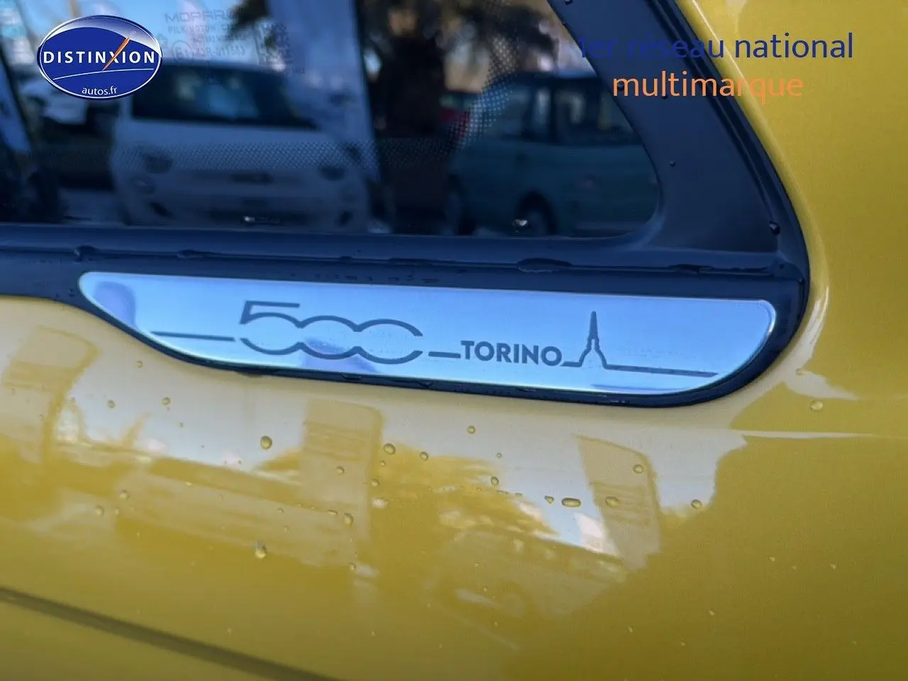 Détail du logo 500 Torino sur la portière jaune gold métal d'une Fiat 500 hybride.