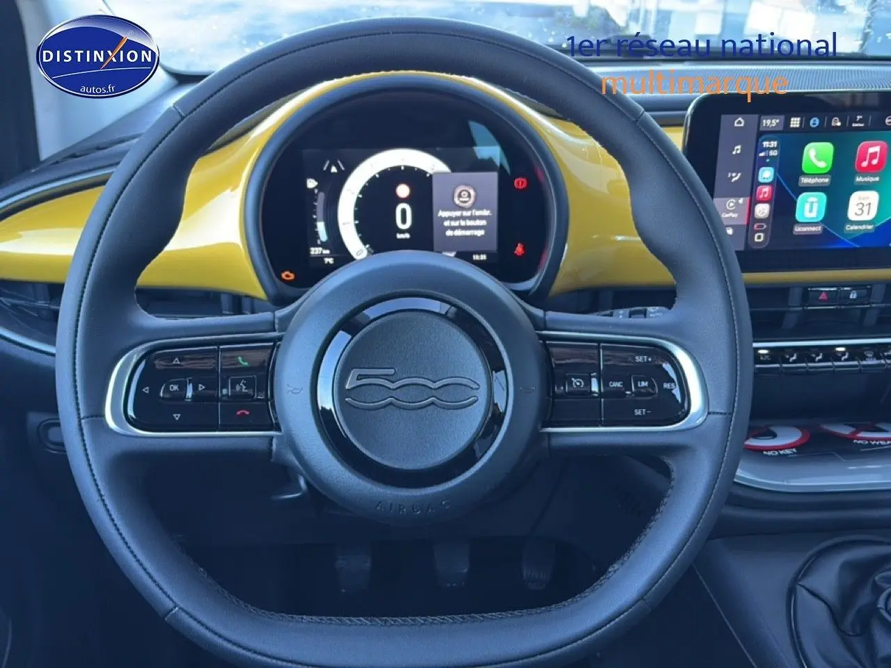 Vue centrée sur le volant noir et tableau de bord jaune or métallisé de la Fiat 500 hybrid avec écran tactile multifonction.