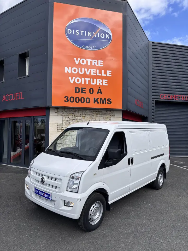 Fourgon électrique DFSK EC35 blanc vu en 3/4 avant droit devant un bâtiment avec enseigne orange Distinxion.