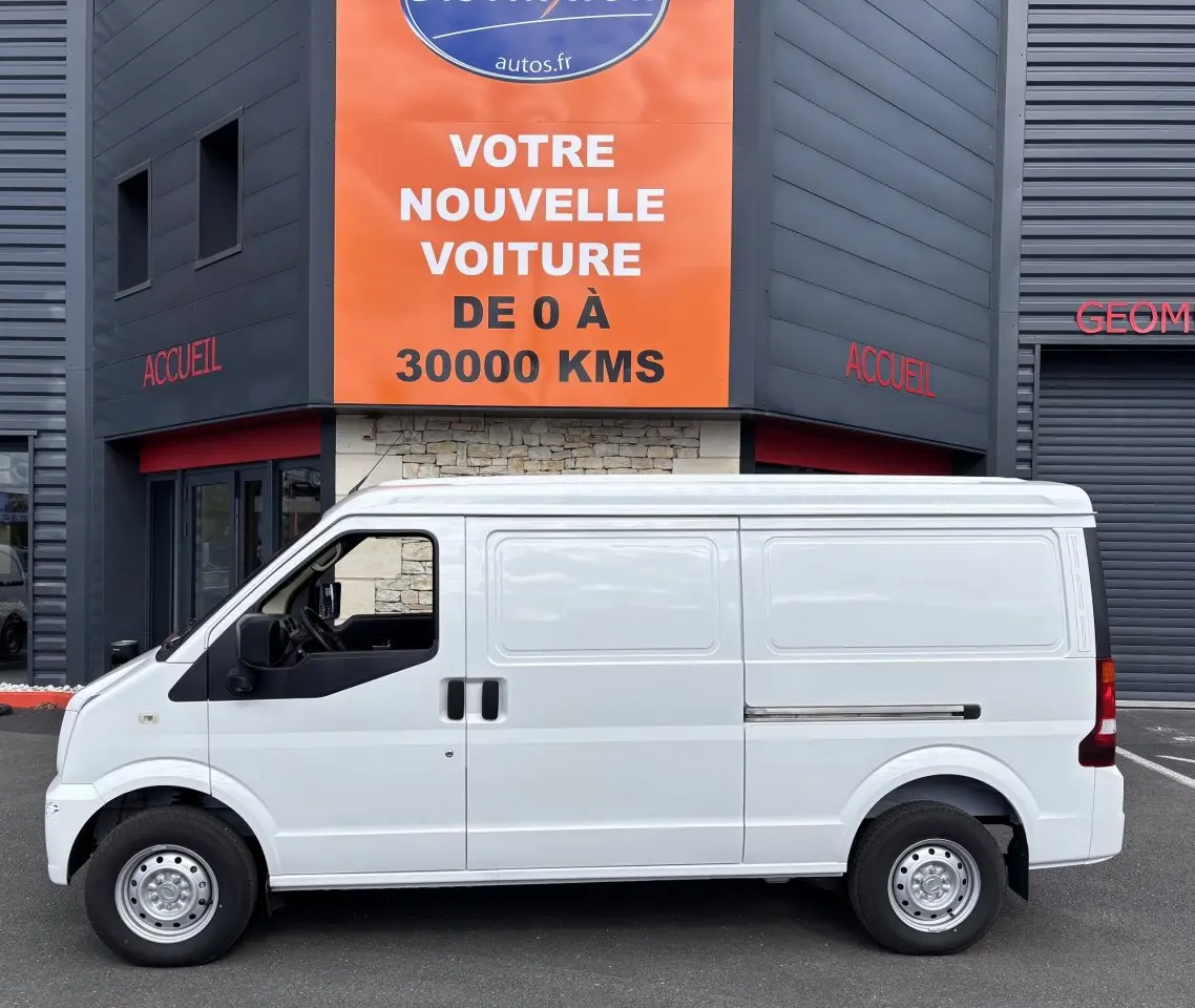 Profil latéral gauche d'un utilitaire blanc DFSK EC35 électrique 2023, sans fenêtres latérales, stationné devant un bâtiment.