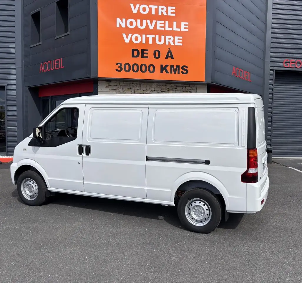 Vue de profil côté gauche du fourgon électrique blanc DFSK EC35 BEV 39KWH, stationné devant un bâtiment commercial.