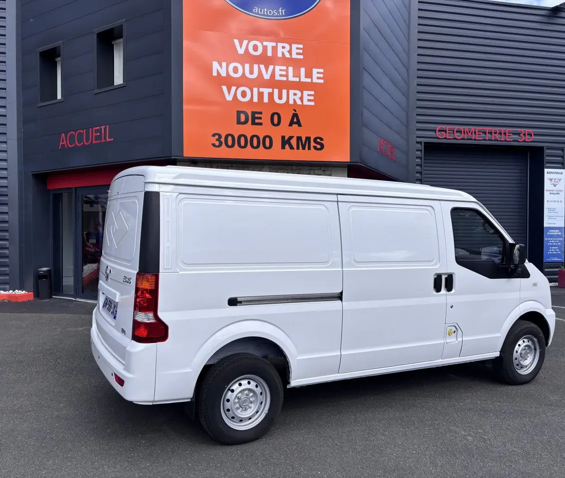 Vue 3/4 arrière droite d'un utilitaire blanc DFSK EC35 électrique stationné devant un bâtiment commercial.