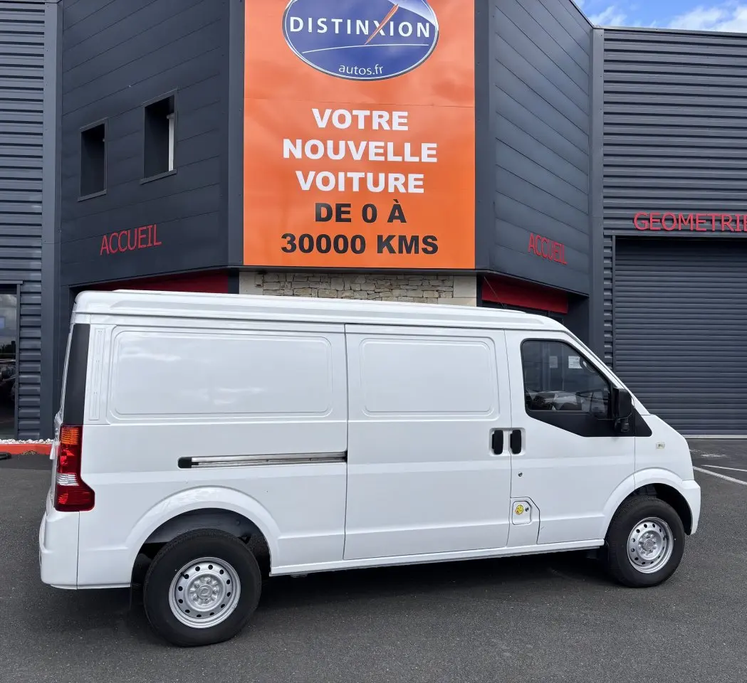 Vue latérale droite d'un utilitaire blanc DFSK EC35 électrique stationné devant un bâtiment commercial.