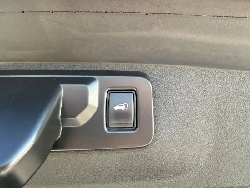 Bouton d'ouverture électrique du coffre sur la garniture intérieure d'une Renault Rafale bleu sommet métallisé.