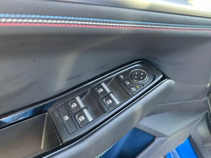 Gros plan sur la commande des vitres électriques côté conducteur avec surpiqûres tricolores sur la porte du Renault Rafale bleu sommet.