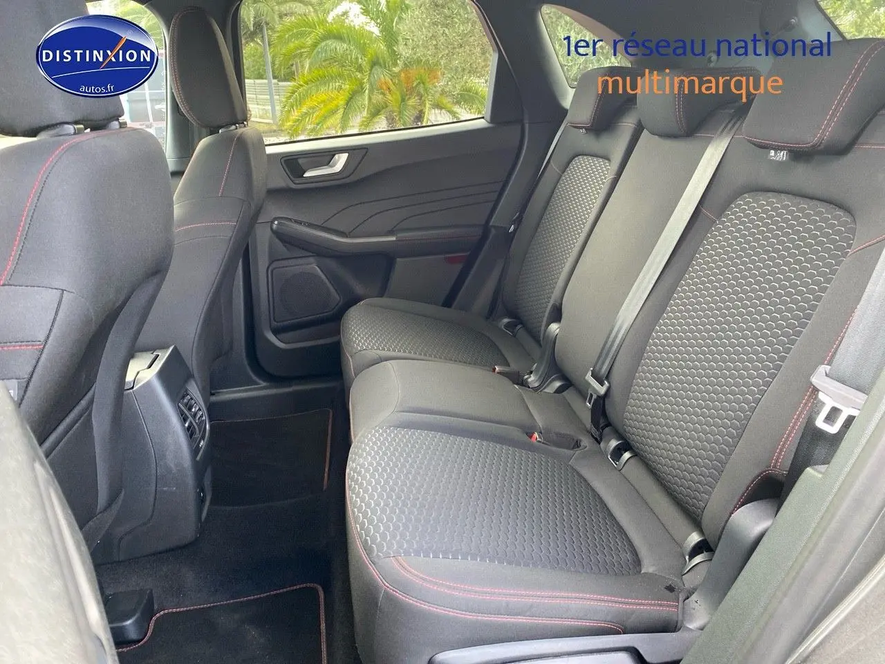 Vue intérieure arrière droite du Ford Kuga 2025, montrant la banquette tissu gris avec surpiqûres rouges et portes ouvertes.