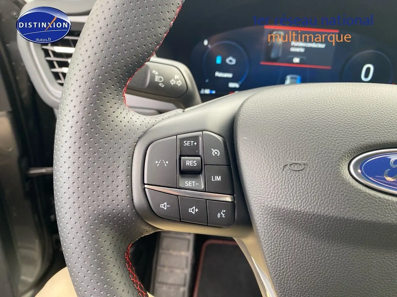 Gros plan sur le volant perforé avec surpiqûres rouges du Ford Kuga 2025, boutons multifonctions visibles.