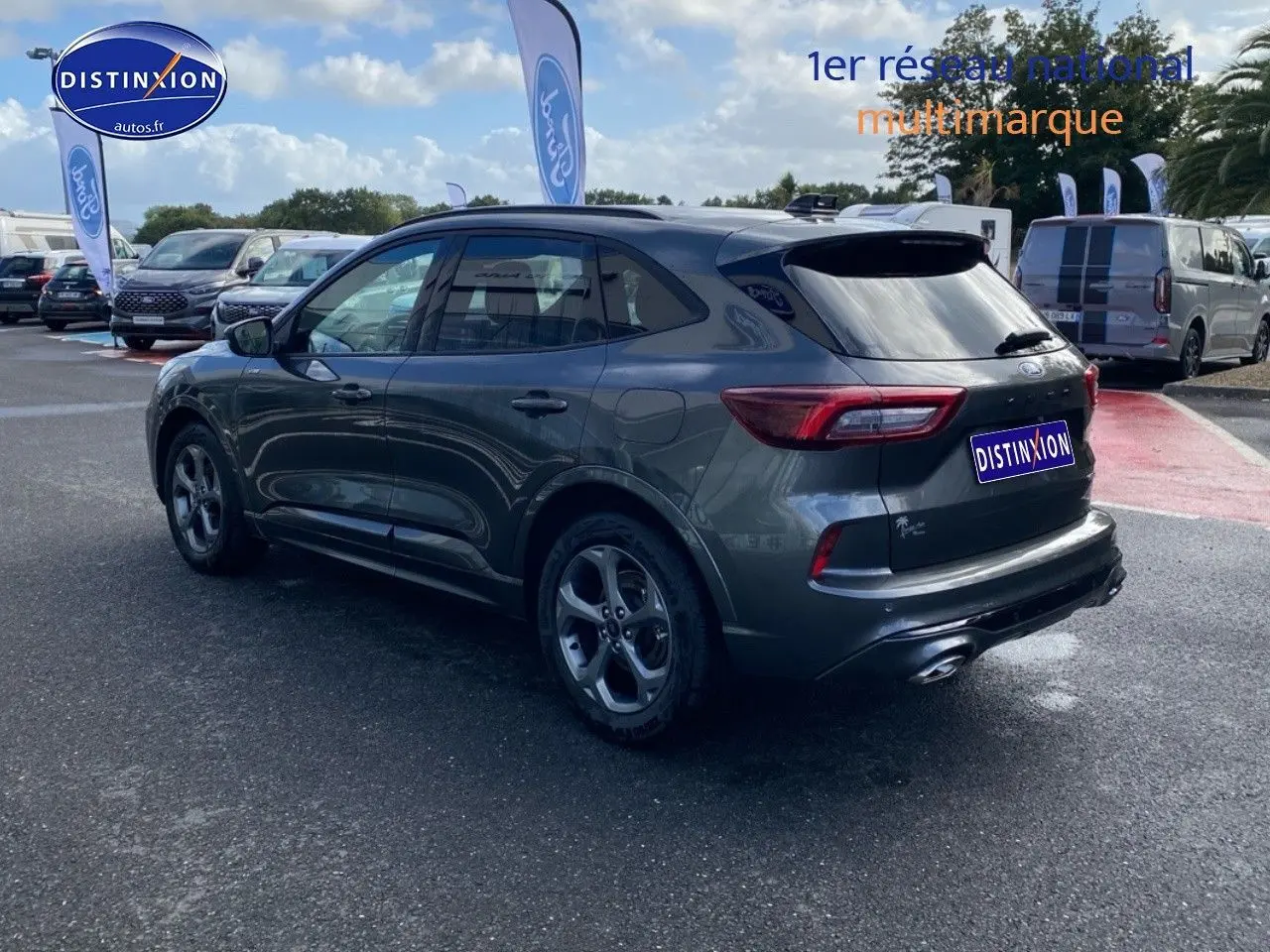 Ford Kuga gris métallisé vu en 3/4 arrière droit, avec jantes alu et feux arrière LED dans un parking extérieur.