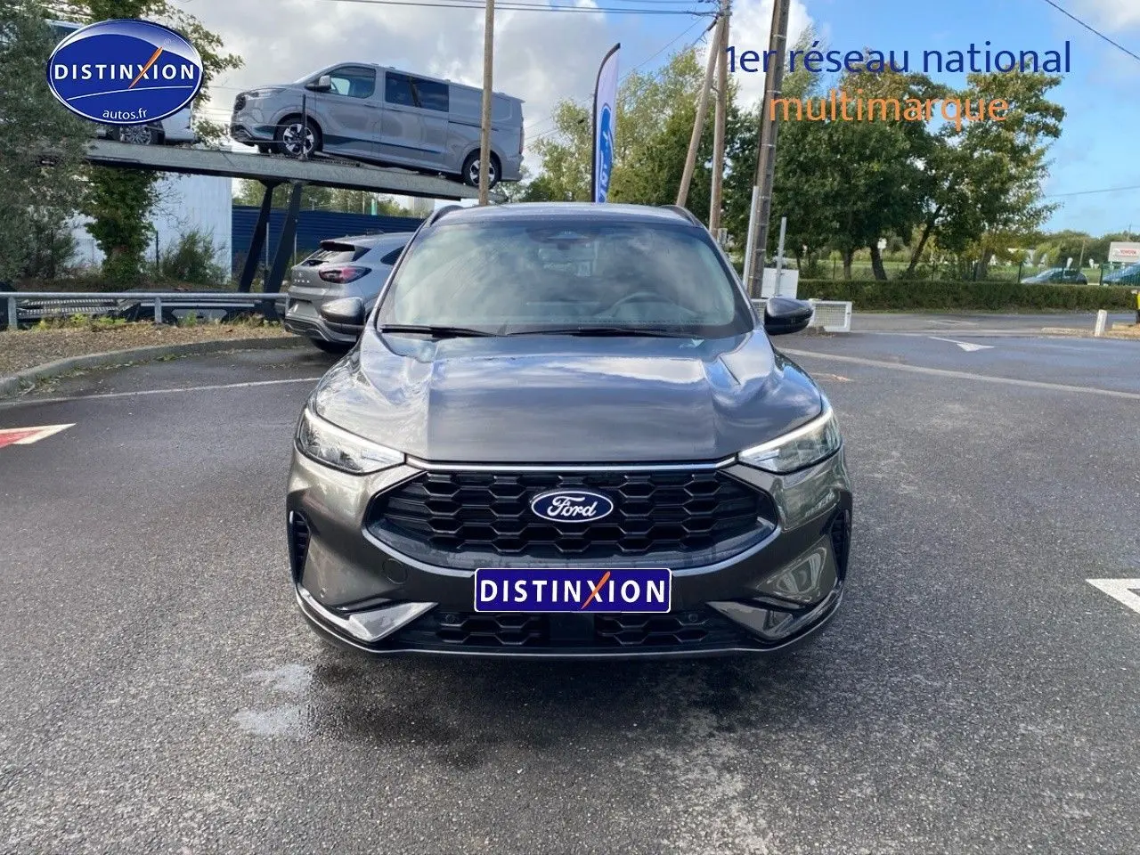 Vue avant d'un Ford Kuga gris métallisé avec calandre noire et phares LED, stationné sur un parking extérieur.