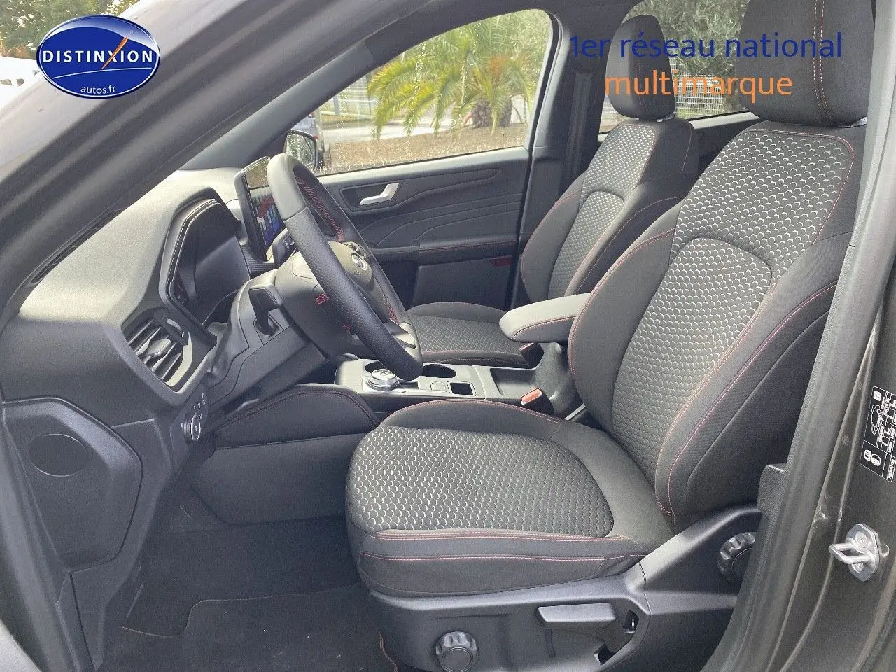 Vue intérieure côté conducteur du Ford Kuga 2025, sièges tissu gris avec surpiqûres rouges et volant multifonction.