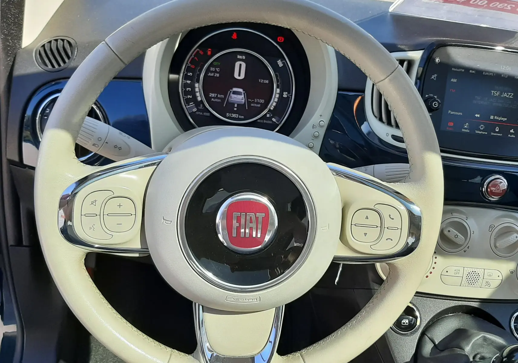 Vue rapprochée du volant beige clair de la Fiat 500 1.2 8V 69 Lounge 2018 avec tableau de bord numérique et console centrale.