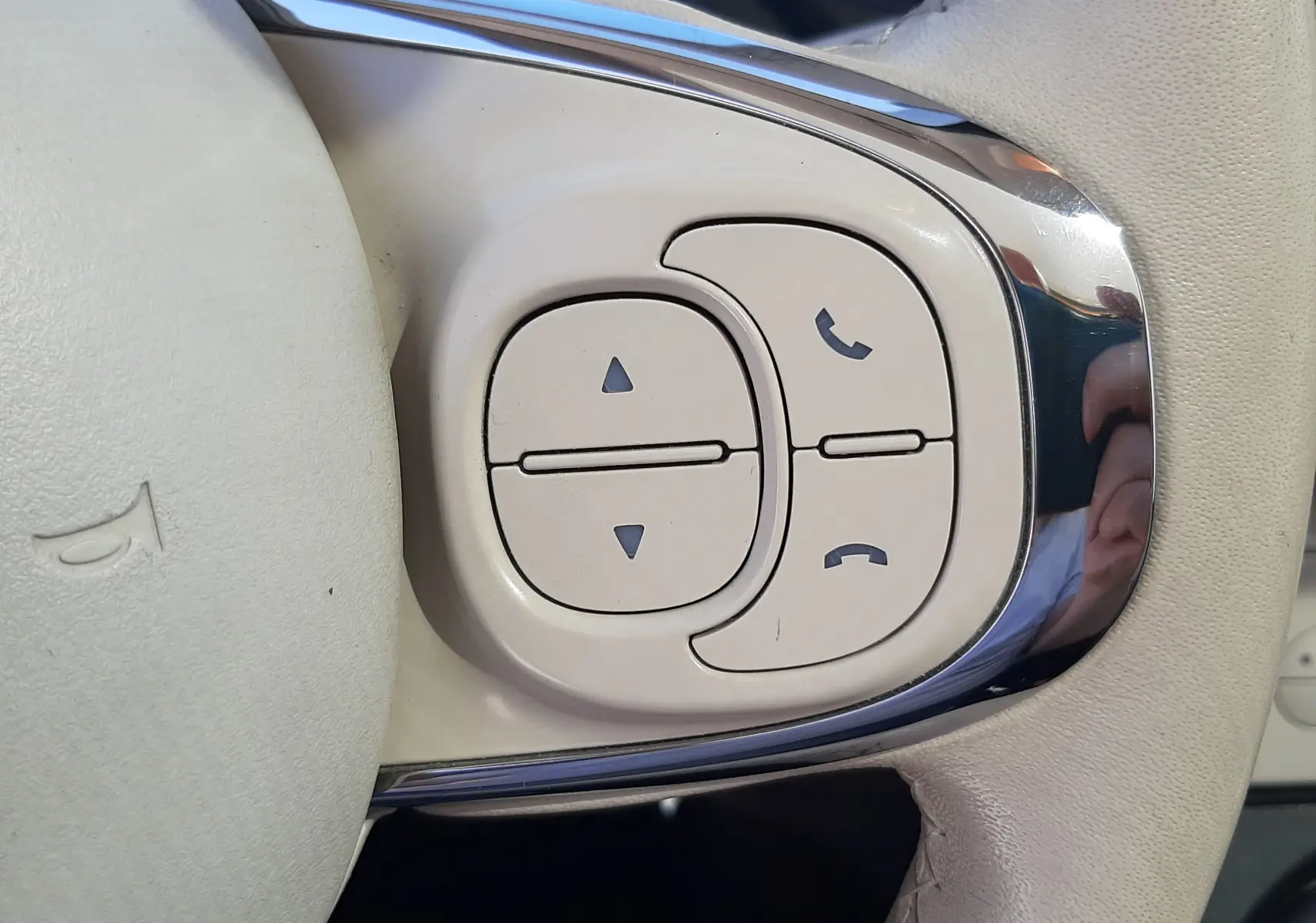 Gros plan sur les commandes beiges du volant de la FIAT 500 Lounge 2018, avec boutons de téléphone et réglages audio.