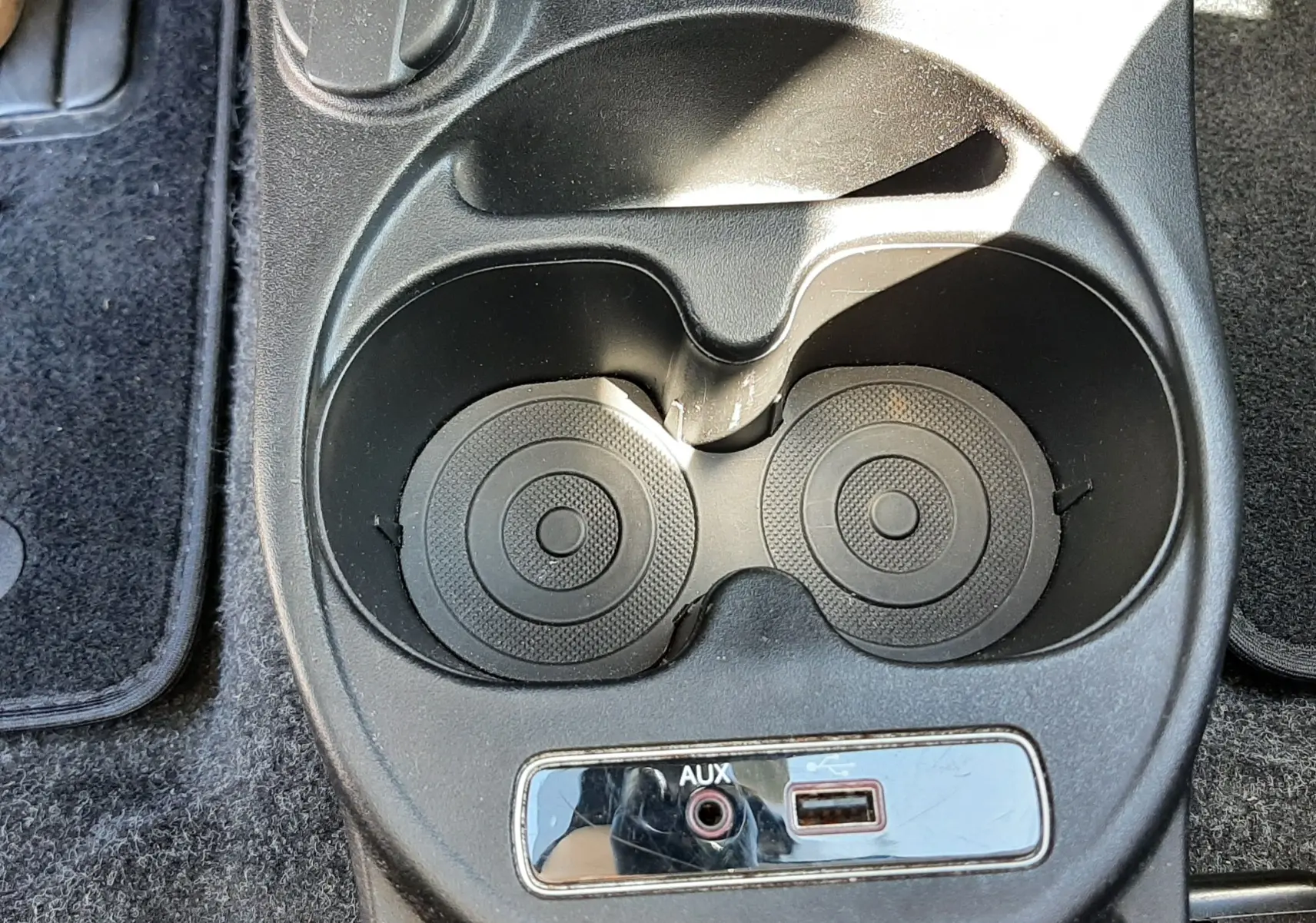 Gros plan sur la console centrale noire de la Fiat 500 bleu, montrant porte-gobelets, prise 12V, port AUX et USB.