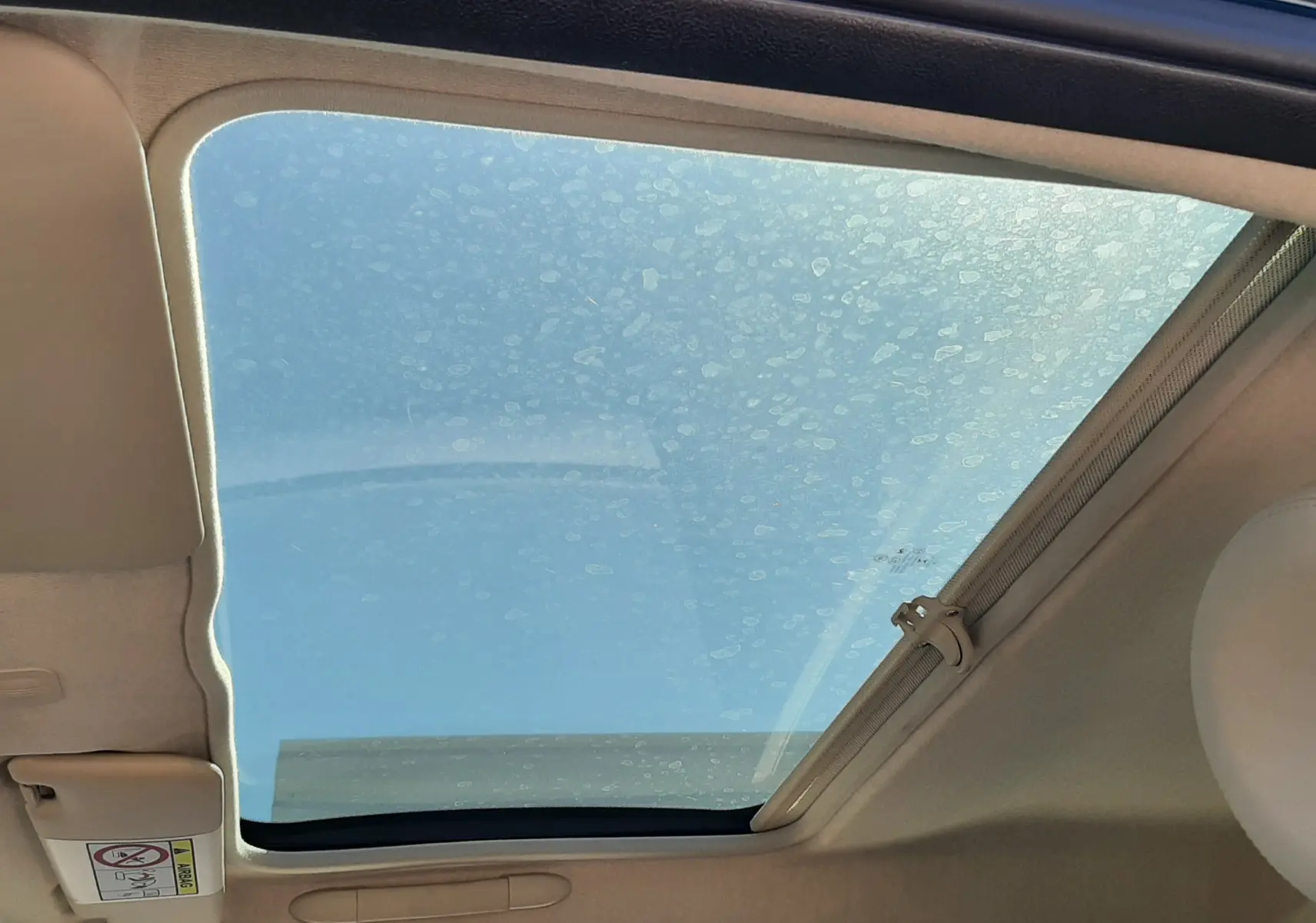 Toit ouvrant panoramique ouvert sur l'intérieur beige d'une FIAT 500 bleue, vue côté conducteur vers le ciel.