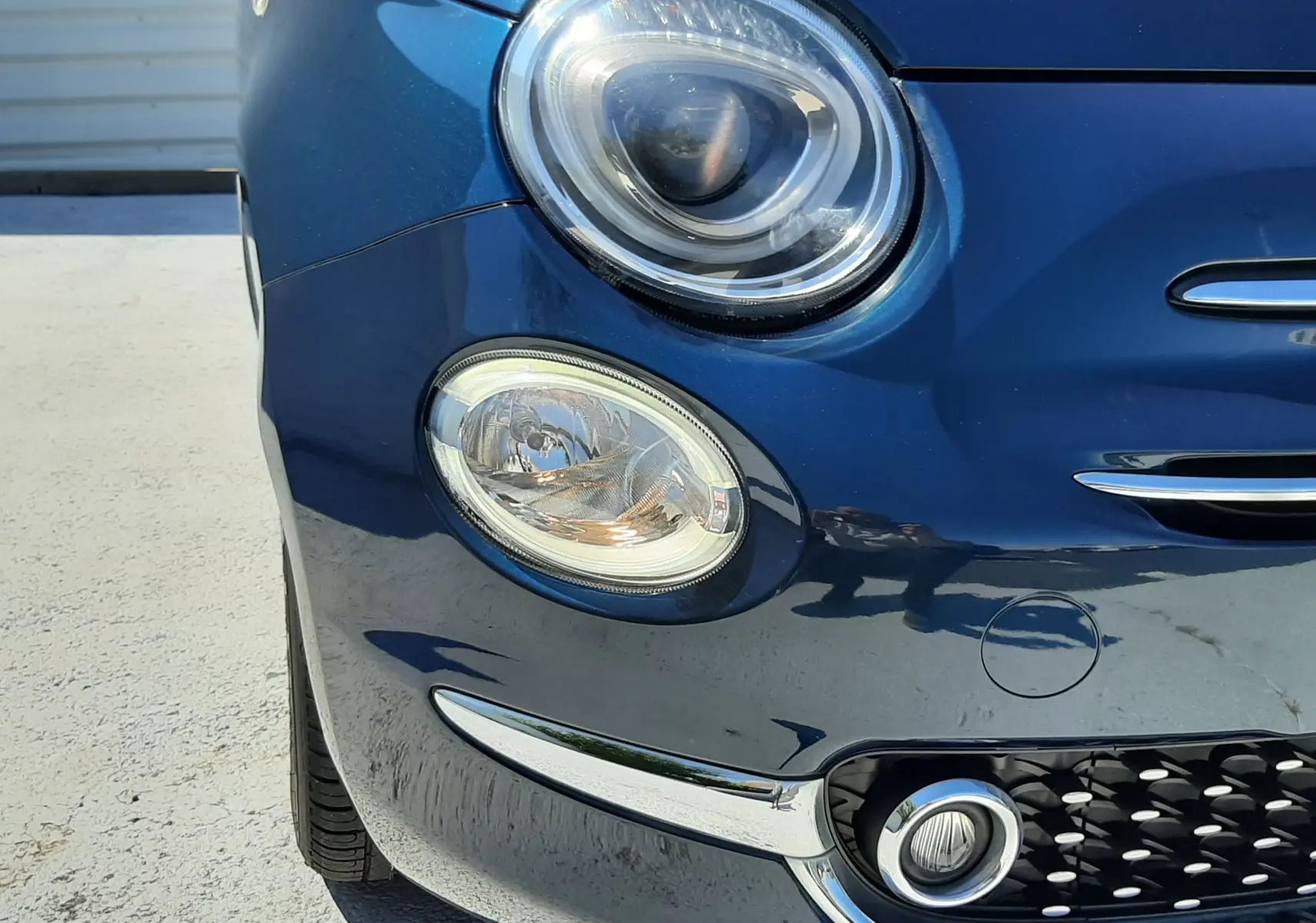 Gros plan sur l’avant droit d’une FIAT 500 bleu métallisé, mettant en valeur ses phares ronds et la calandre chromée.