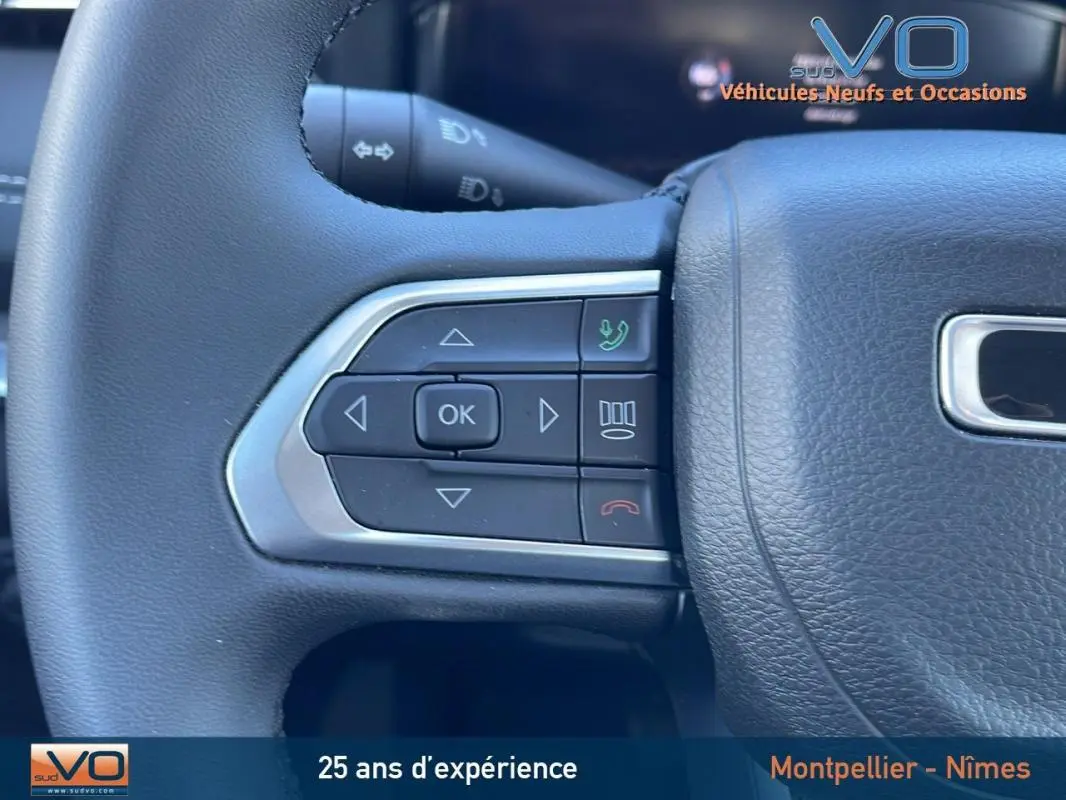 Gros plan sur les commandes gauche du volant noir du Jeep Compass blanc 2024 avec boutons multifonctions intégrés.