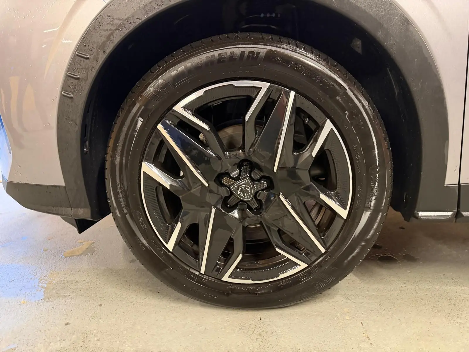 Gros plan sur la roue avant droite du Peugeot 3008 gris 1.2 Hybrid 136 avec jante noire et argentée au design moderne.