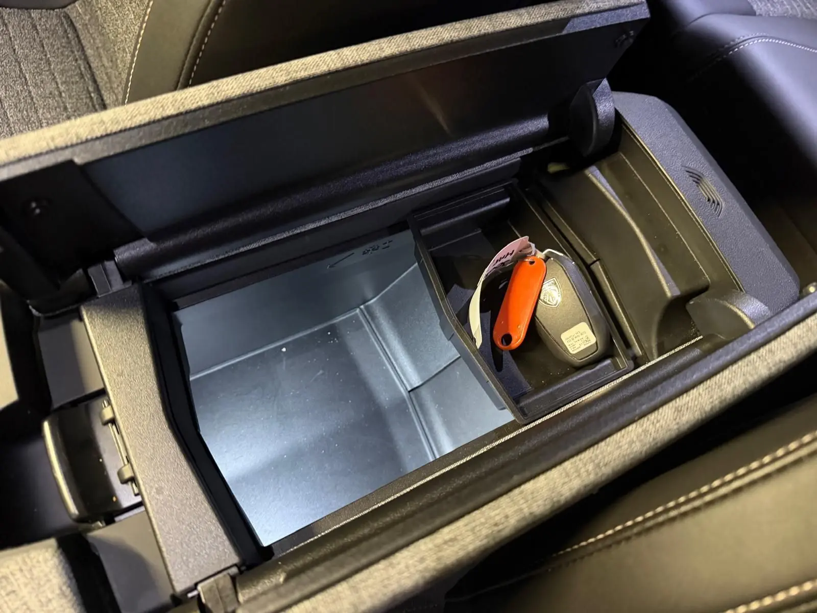 Vue plongeante sur le rangement central noir du Peugeot 3008 gris avec clé et porte-clés orange à l’intérieur.